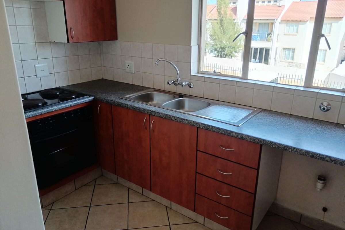 A functional kitchen featuring wood-finish cabinetry, laminate countertops, a double sink, and built-in electric cooking appliances with tiled flooring.