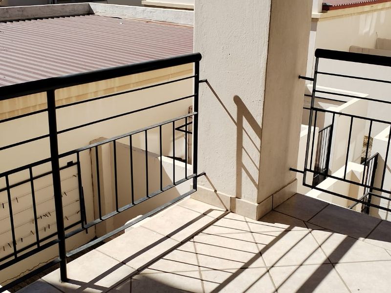 A private balcony featuring tiled flooring and a secure metal balustrade, overlooking the surrounding residential complex.