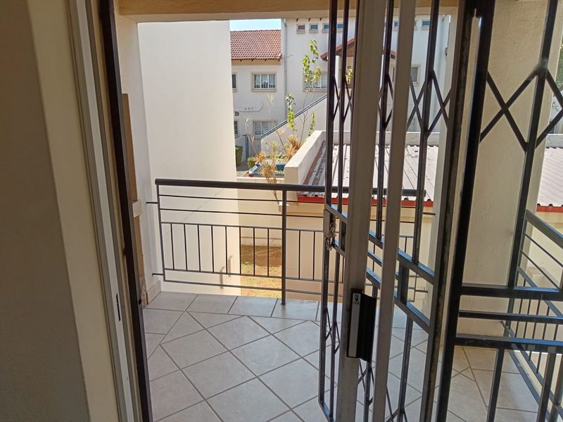 A functional balcony featuring tiled flooring, a metal balustrade, and a secure metal gate, offering an outdoor space with views of the surrounding complex.