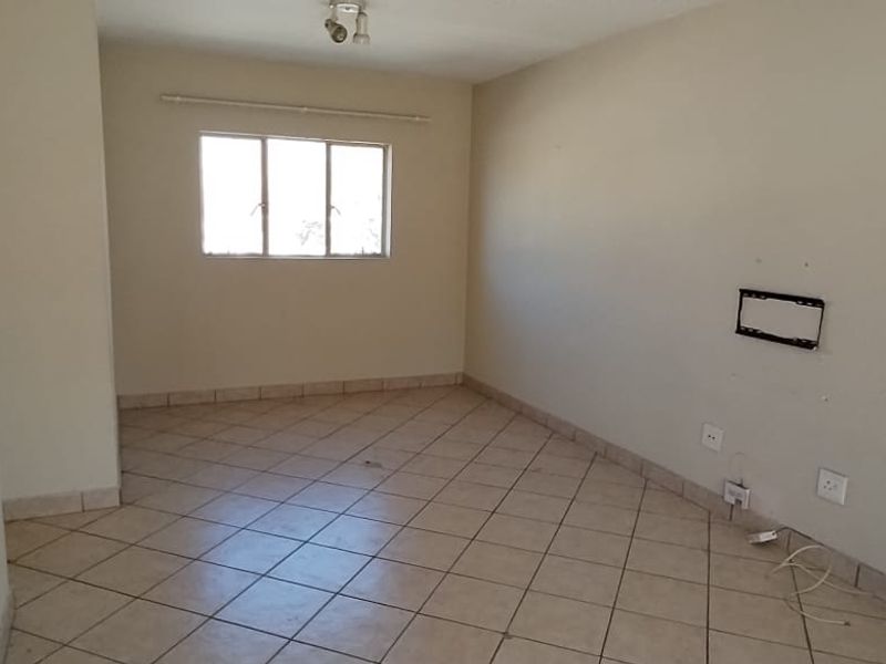 An empty living room featuring tiled flooring, an intercom system, and neutral wall finishes, providing a blank canvas for potential interior design updates.