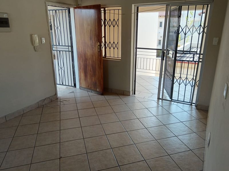 An empty living area featuring tiled flooring, an intercom system, and direct access to an outdoor balcony through a sliding door with security gates.