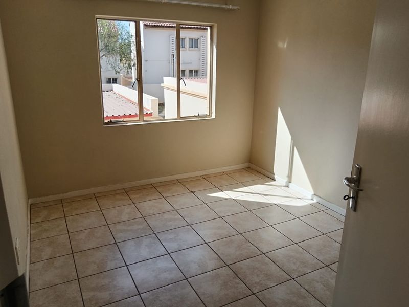 A bright, empty bedroom featuring neutral tiled flooring and a large window, providing a clean and versatile space ready for personalization.