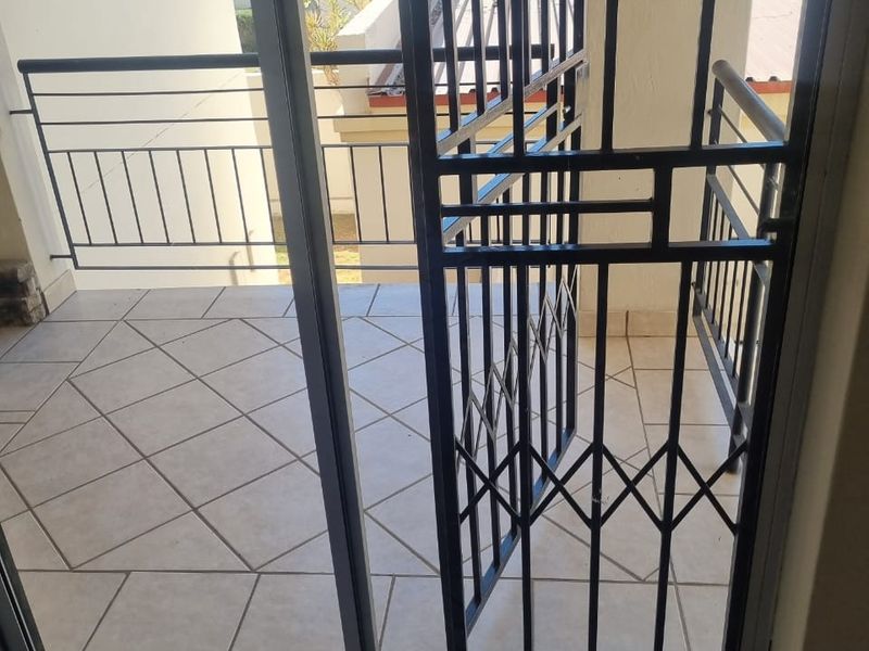 A tiled balcony featuring a metal security gate and balustrade, offering an outdoor space accessible through a sliding glass door.