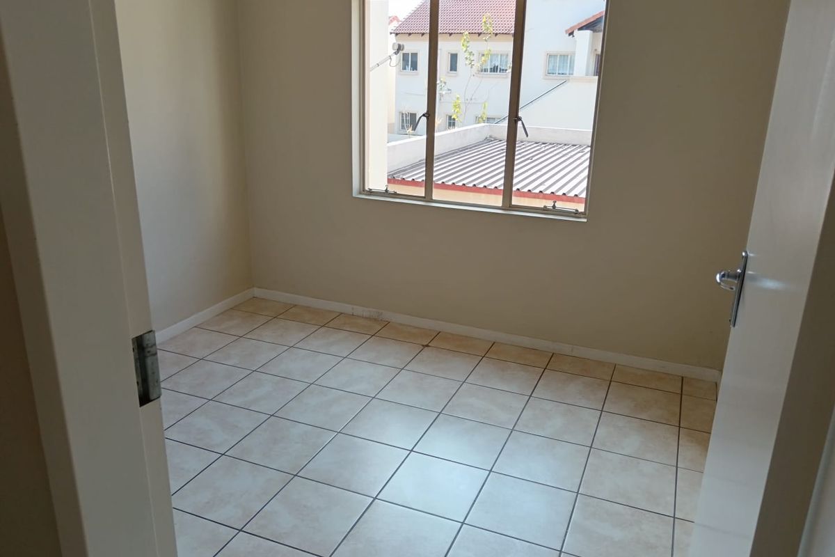 An empty bedroom featuring neutral wall paint, tiled flooring, and an aluminium-framed window overlooking the surrounding residential area.