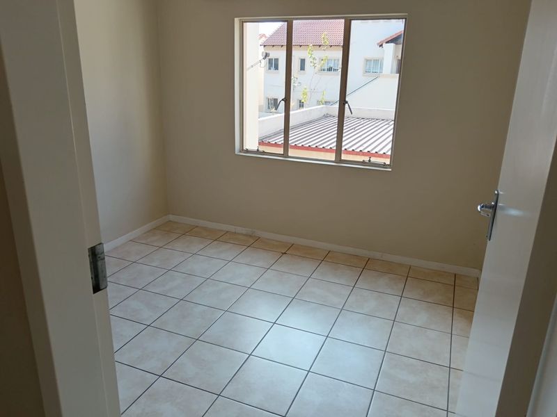 An empty bedroom featuring neutral wall paint, tiled flooring, and an aluminium-framed window overlooking the surrounding residential area.
