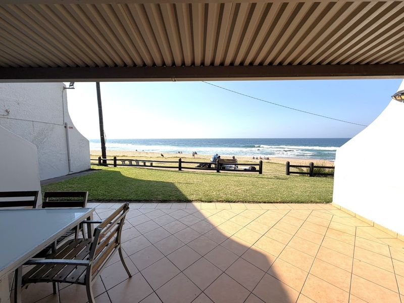 A covered patio area featuring tiled flooring and direct access to a private lawn with unobstructed ocean and beach views.