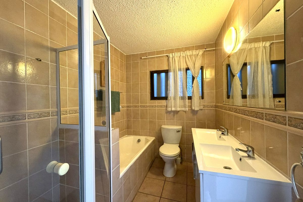 A functional bathroom featuring a double vanity, built-in bathtub, separate shower enclosure, and neutral wall tiling.