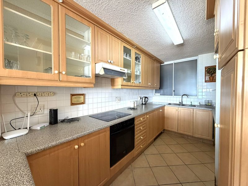 A functional kitchen featuring light wood cabinetry, laminate countertops, a tiled backsplash, and integrated appliances, offering a classic layout with ample storage space.