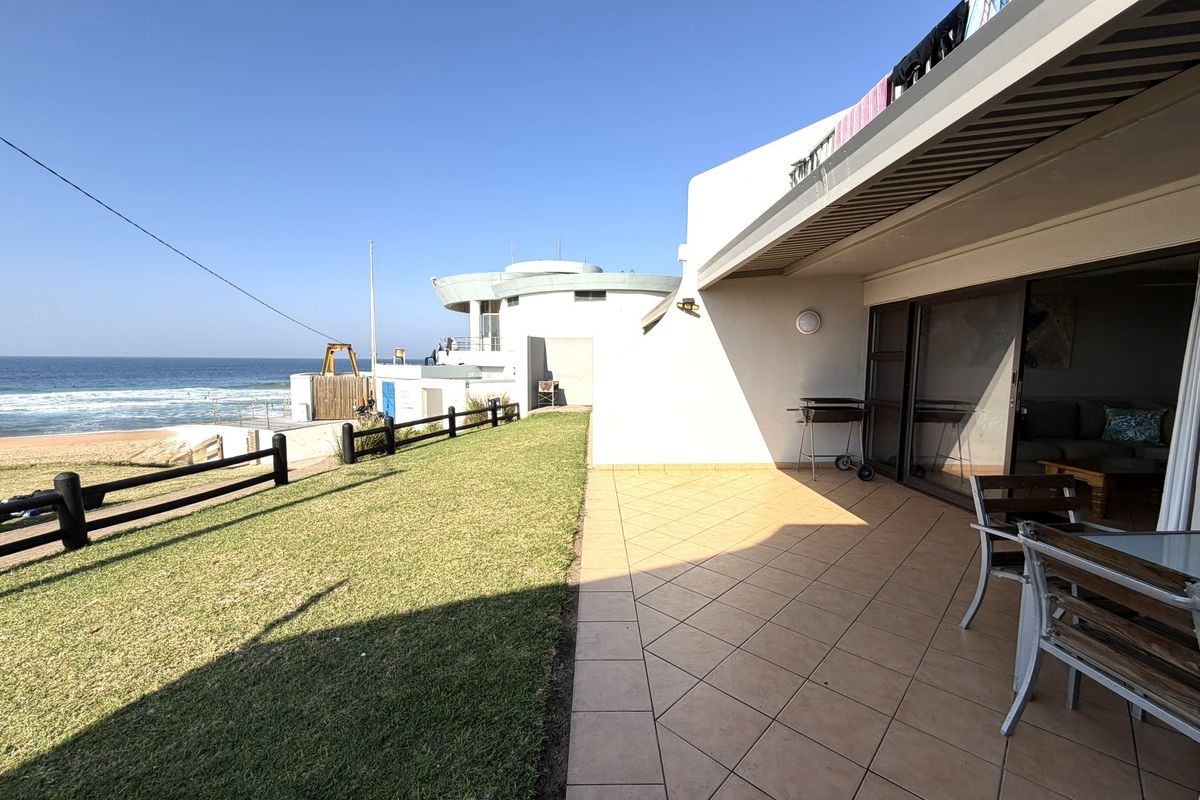 A spacious tiled patio area featuring sliding glass doors, outdoor lighting, and direct access to a lawn with ocean views.