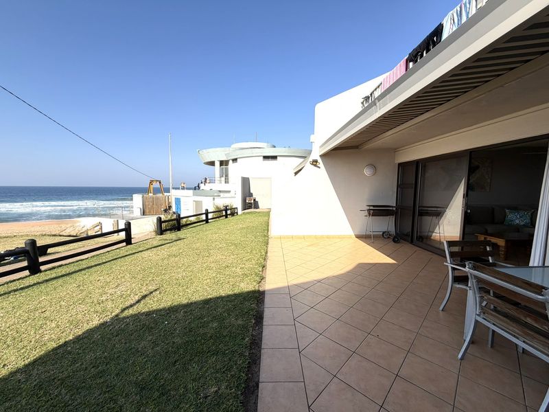 A spacious tiled patio area featuring sliding glass doors, outdoor lighting, and direct access to a lawn with ocean views.