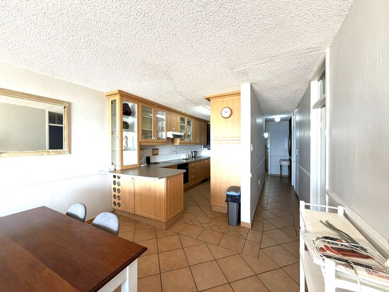 Open plan kitchen and dining area featuring wooden cabinetry, tiled flooring, and a textured ceiling, offering a functional layout with potential for modern updates.