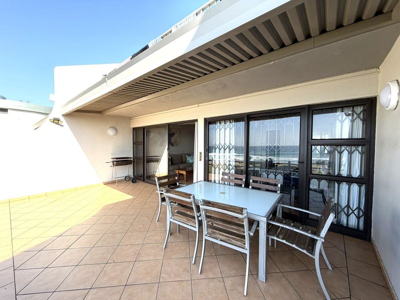 Spacious covered balcony featuring tiled flooring, sliding glass doors with security gates, and direct access to the living area with ocean views.