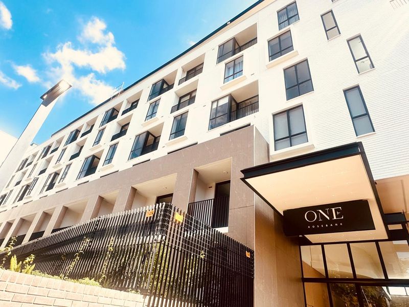 A low-angle view of the modern One Rosebank apartment building facade, featuring clean architectural lines, balconies, and a prominent entrance canopy.