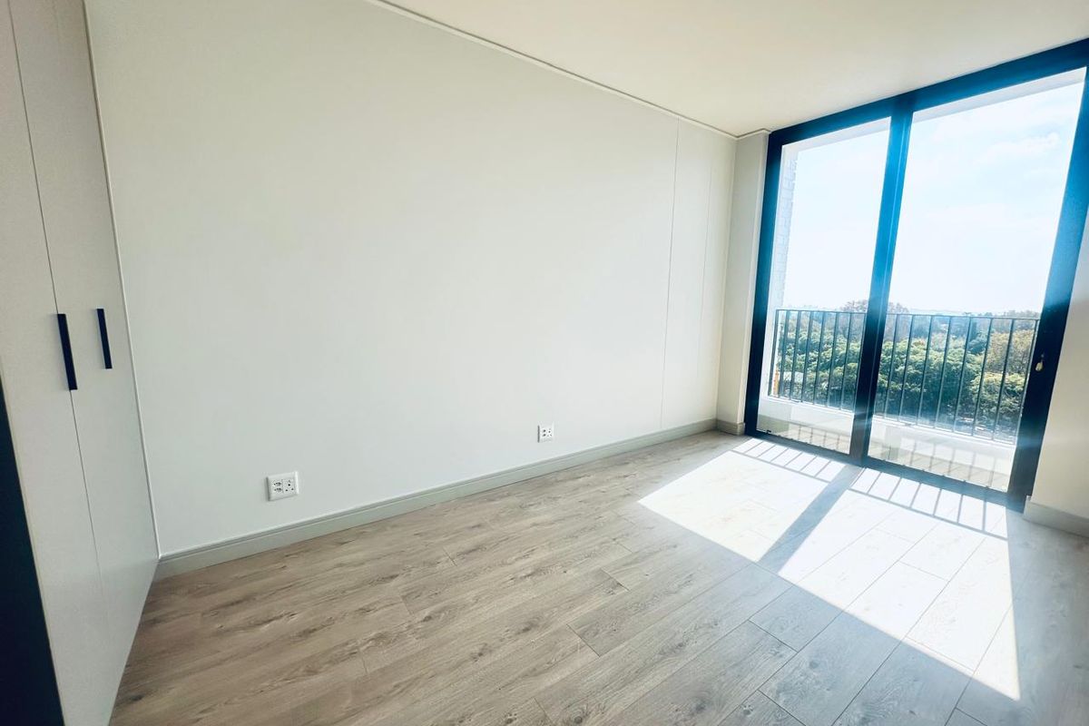 A bright, empty bedroom featuring modern laminate flooring, a built-in wardrobe, and large sliding glass doors leading to a balcony with scenic views.