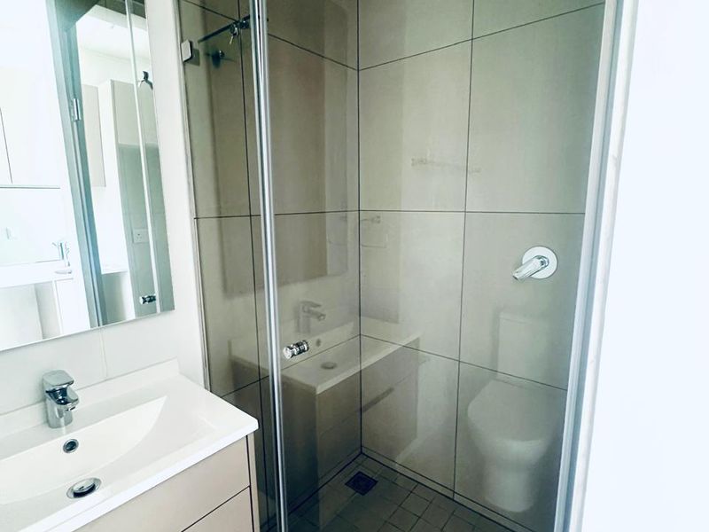 Modern bathroom featuring a vanity with basin, wall-mounted mirror, and a glass-enclosed shower with a rain shower head and neutral tiling.