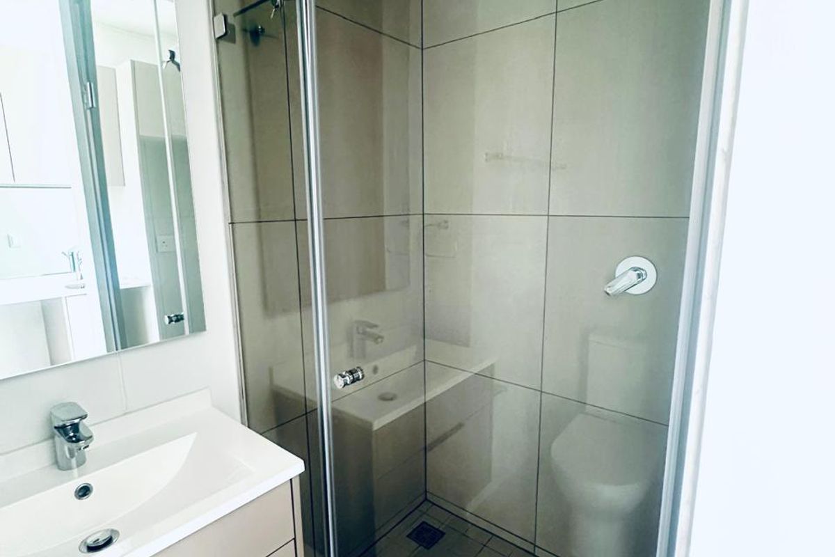 Modern bathroom featuring a vanity with basin, wall-mounted mirror, and a glass-enclosed shower with a rain shower head and neutral tiling.