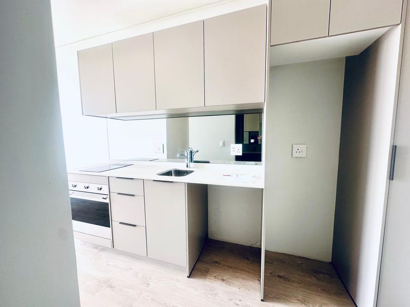 Modern compact kitchen featuring neutral cabinetry, built-in oven and hob, stainless steel sink, and a reflective mirror splashback.