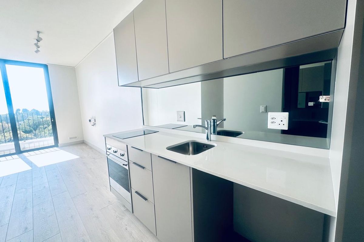 Modern open-plan kitchen featuring sleek cabinetry, stone countertops, integrated appliances, and a mirrored splashback, leading to a bright living area with balcony access.