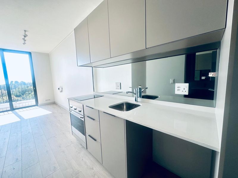 Modern open-plan kitchen featuring sleek cabinetry, stone countertops, integrated appliances, and a mirrored splashback, leading to a bright living area with balcony access.