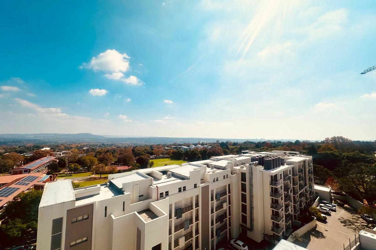 An elevated aerial view of a modern multi-story apartment complex featuring balconies and an adjacent parking area, set against a scenic landscape.
