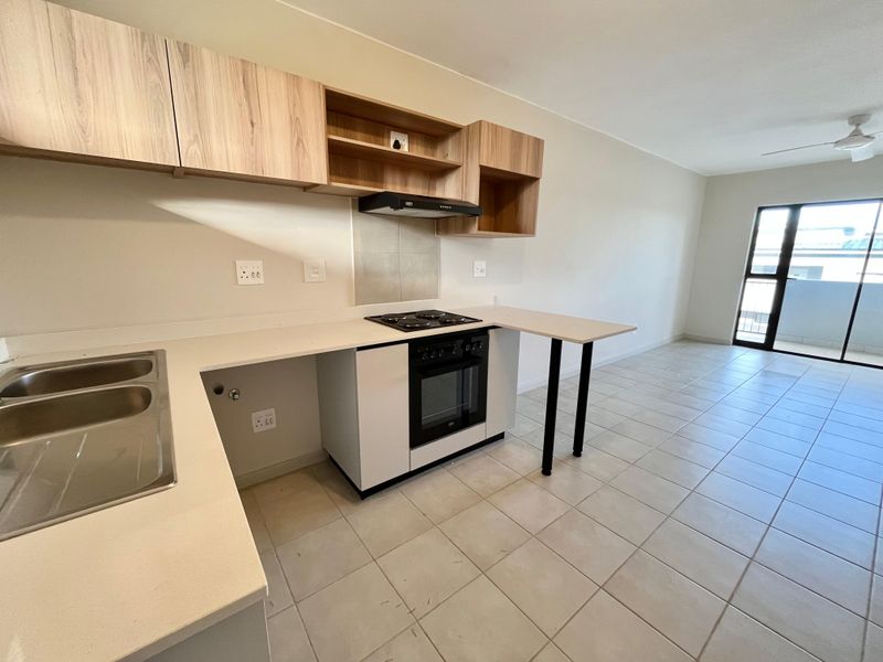 Modern open-plan kitchen and living area featuring light wood cabinetry, built-in oven and hob, tiled flooring, and access to a balcony.