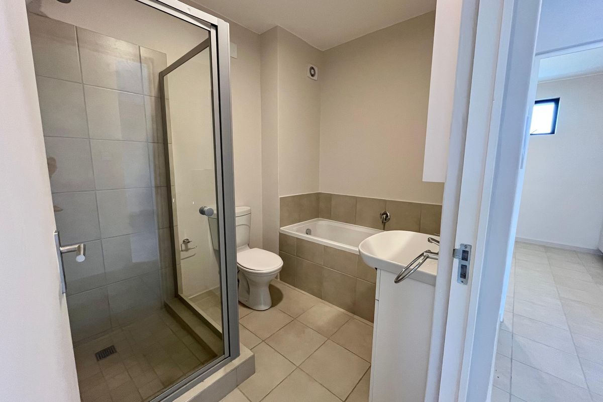 A clean, functional bathroom featuring a separate shower enclosure, bathtub, toilet, and vanity basin with neutral tiled finishes.