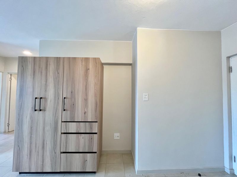 A clean, empty bedroom featuring modern wood-finish built-in wardrobes and neutral tiled flooring, providing a versatile space ready for personalization.