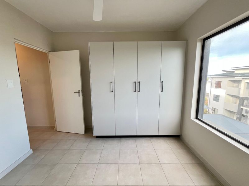 A bright, empty bedroom featuring neutral tiled flooring, a large built-in wardrobe, and a ceiling fan, offering a clean and versatile living space.