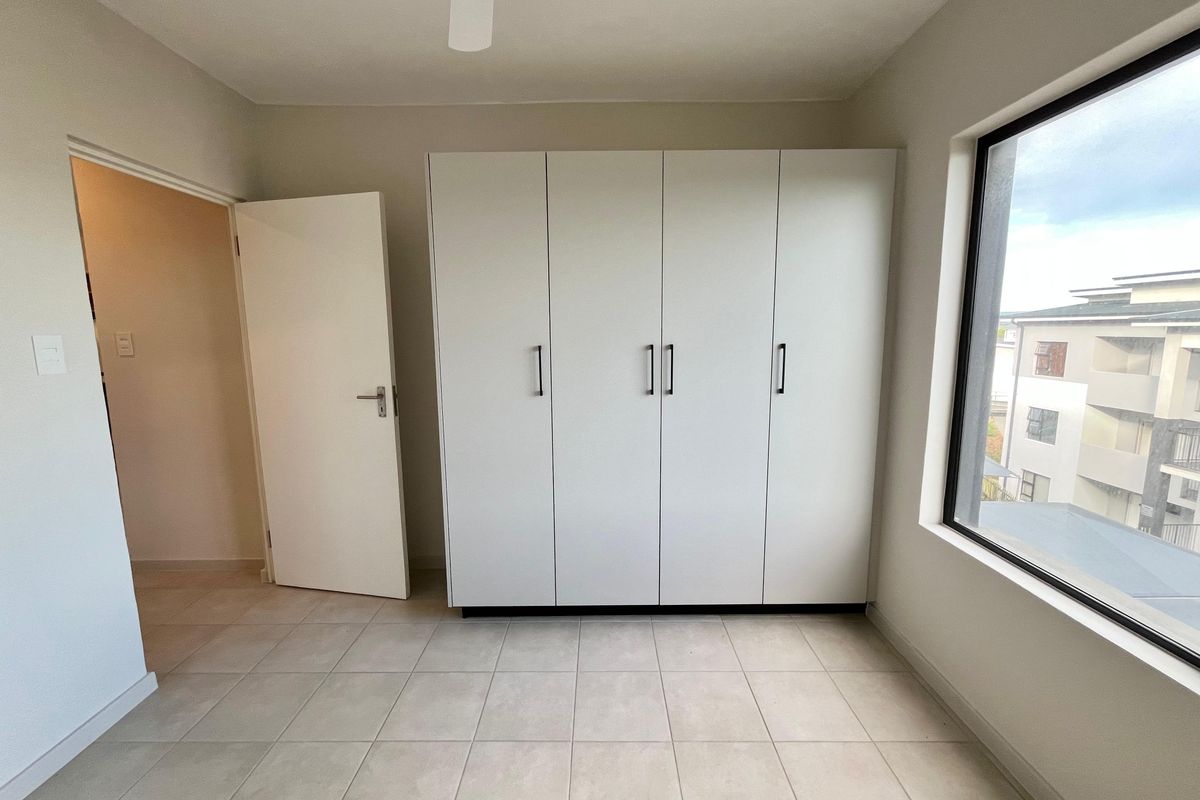 A bright, empty bedroom featuring neutral tiled flooring, a large built-in wardrobe, and a ceiling fan, offering a clean and versatile living space.