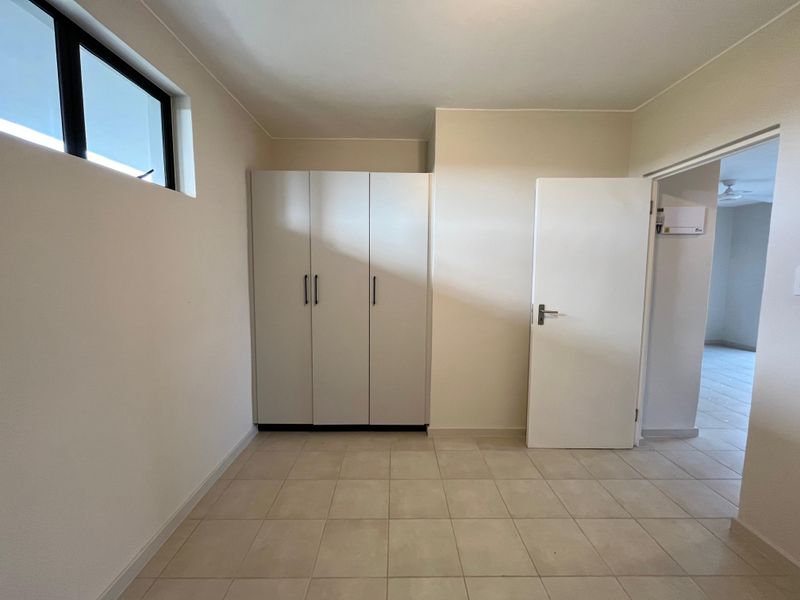 A clean, empty bedroom featuring neutral tiled flooring, a built-in wardrobe, and a high-level window providing natural light.