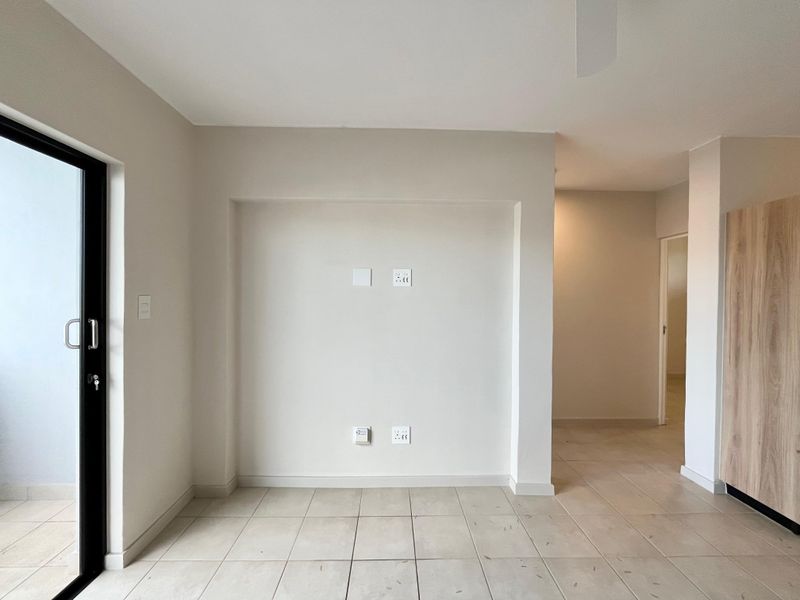 A bright, empty living area featuring neutral tiled flooring, a modern sliding glass door, and built-in cabinetry, ready for personalization.