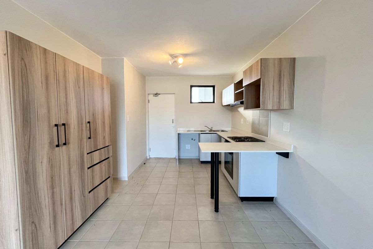 A clean, empty kitchen featuring light wood-look cabinetry, white countertops, a built-in oven, hob, and tiled flooring.