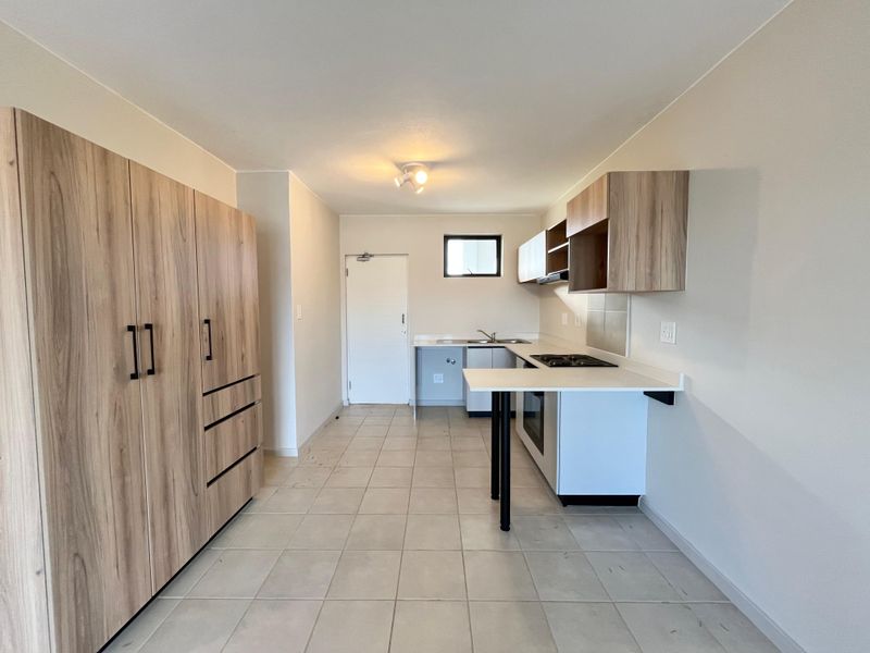 A clean, empty kitchen featuring light wood-look cabinetry, white countertops, a built-in oven, hob, and tiled flooring.