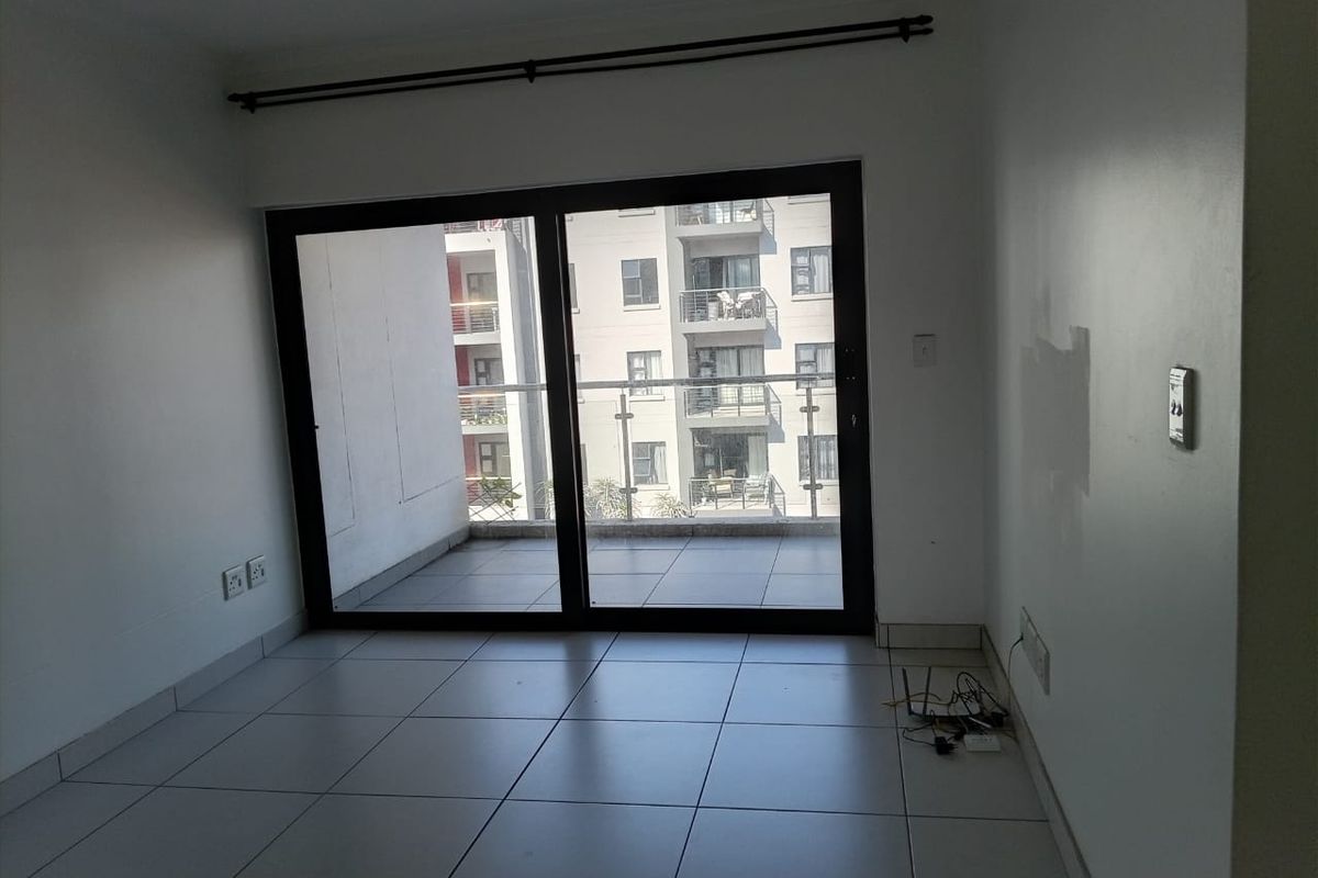 An empty living room featuring tiled flooring and a large sliding glass door that opens onto a balcony.