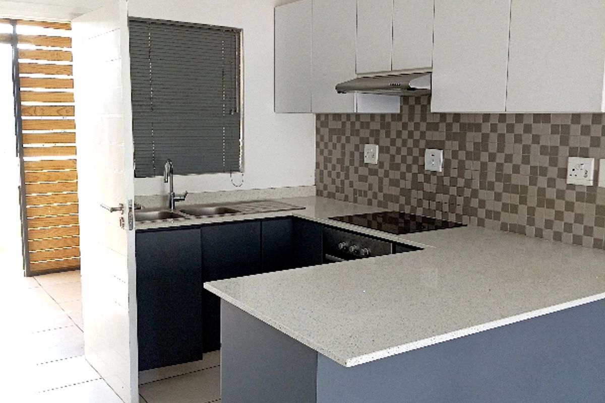 Modern kitchen featuring white and dark grey cabinetry, stone countertops, tiled backsplash, and integrated electric hob with extractor fan.