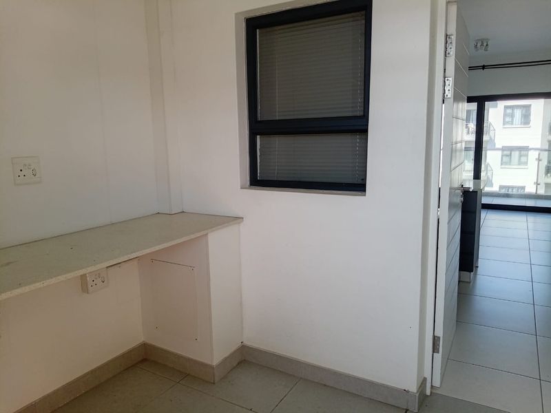 A compact utility space or study nook featuring a built-in desk, tiled flooring, and a window, offering a functional area for work or storage.