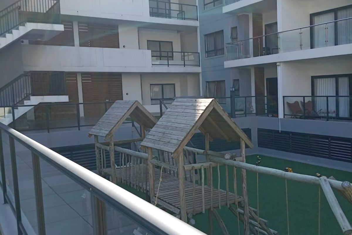 View of a multi-story apartment complex courtyard featuring a tiled patio area, artificial lawn, and external staircases.
