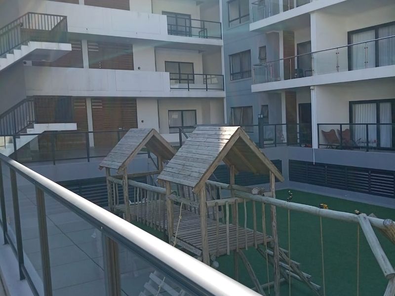 View of a multi-story apartment complex courtyard featuring a tiled patio area, artificial lawn, and external staircases.