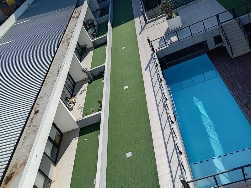 Aerial view of the apartment complex courtyard featuring a swimming pool, paved patio areas, and artificial turf landscaping.