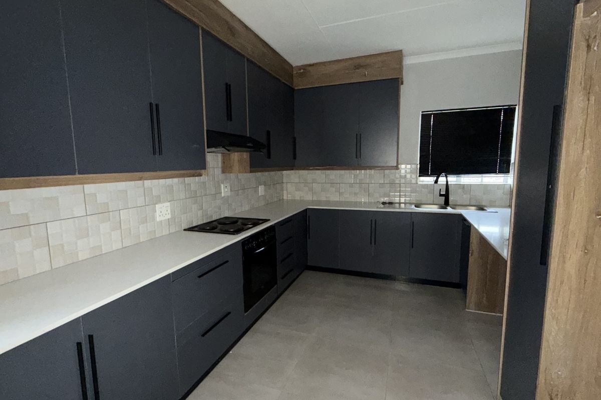 Modern kitchen featuring dark cabinetry, light stone countertops, built-in oven and hob, tiled backsplash, and a double sink with a contemporary mixer tap.