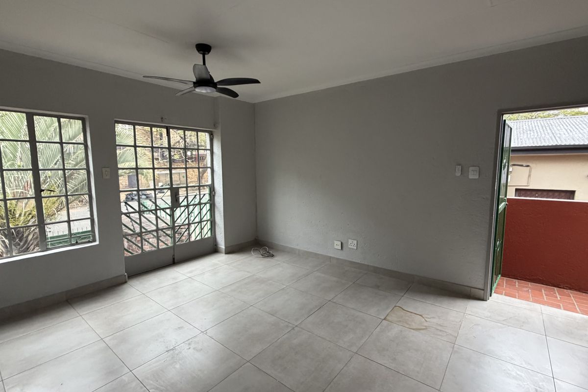 An empty living room featuring neutral tiled flooring, a ceiling fan, and direct access to an outdoor area through security-gated french doors.