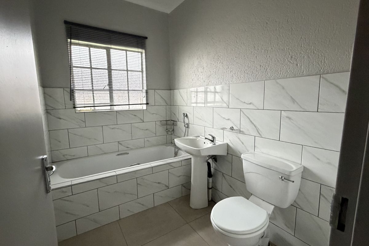 A clean, modern bathroom featuring a bathtub, pedestal sink, toilet, and stylish marble-look wall tiling.