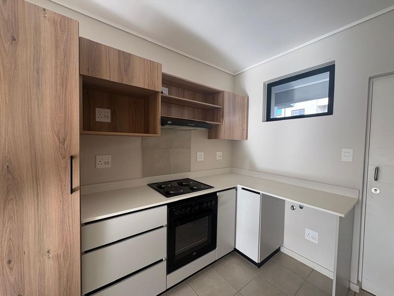 Modern kitchen featuring wood-look and white cabinetry, stone countertops, built-in electric oven and hob, and a dedicated space for an under-counter appliance.