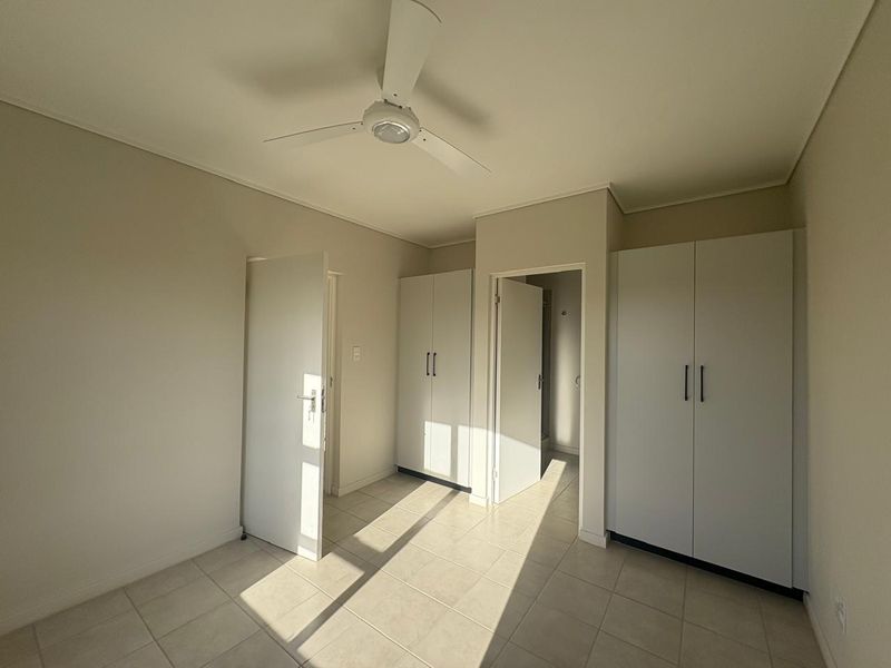 A bright, empty bedroom featuring neutral tiled flooring, a ceiling fan, and ample built-in cupboard storage space.