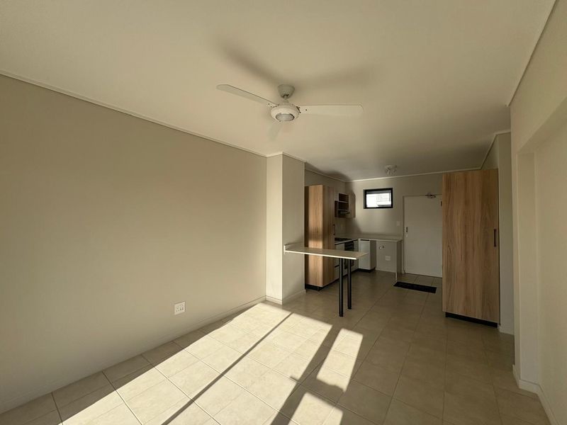 An open-plan living and kitchen area featuring tiled floors, a ceiling fan, built-in cabinetry, and a breakfast bar in a neutral, well-lit space.