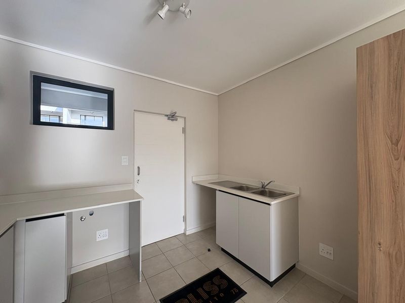 A clean and functional laundry room featuring tiled flooring, built-in cabinetry with a double sink, and dedicated plumbing connections for appliances.