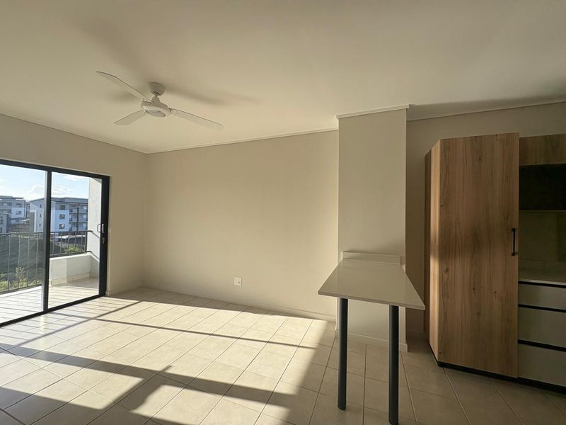 Bright open-plan living area featuring tiled floors, a ceiling fan, built-in cabinetry, and direct access to a private balcony.