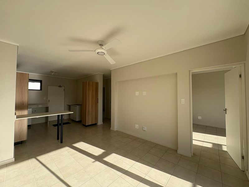 An open-plan living and kitchen area featuring neutral tiled flooring, a ceiling fan, and built-in cabinetry with a breakfast bar.