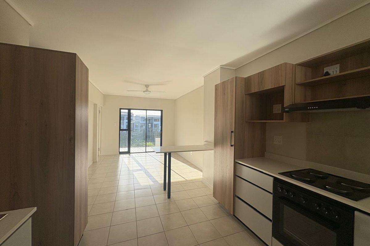 Open-plan kitchen and living area featuring modern built-in cabinetry, integrated appliances, tiled flooring, and access to a balcony through sliding glass doors.