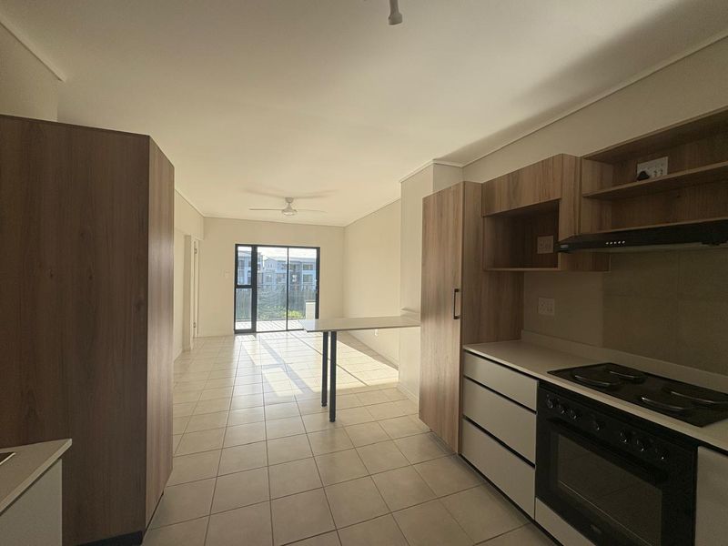 Open-plan kitchen and living area featuring modern built-in cabinetry, integrated appliances, tiled flooring, and access to a balcony through sliding glass doors.